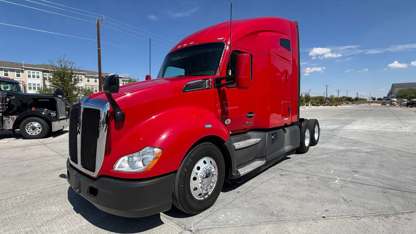 Red Kenworth T680 tractor cab, side view, black front bumper, sleeper cab, large fuel tanks, dual rear axles.