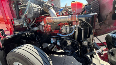 Kenworth truck engine bay showing high-performance fuel lines, turbo, and coolant reservoir with exposed chassis and wheel nearby.