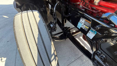 Truck chassis and front suspension of a 2022 Kenworth T680. Visible are the air ride components, frame rails, and warning labels near the front, with parts of the engine and red components in view.