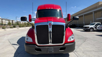 Kenworth T680 front view showing bold black grille, red cab, and large mirrors; daytime outdoor lot; chrome grille surround and bumper area visible.