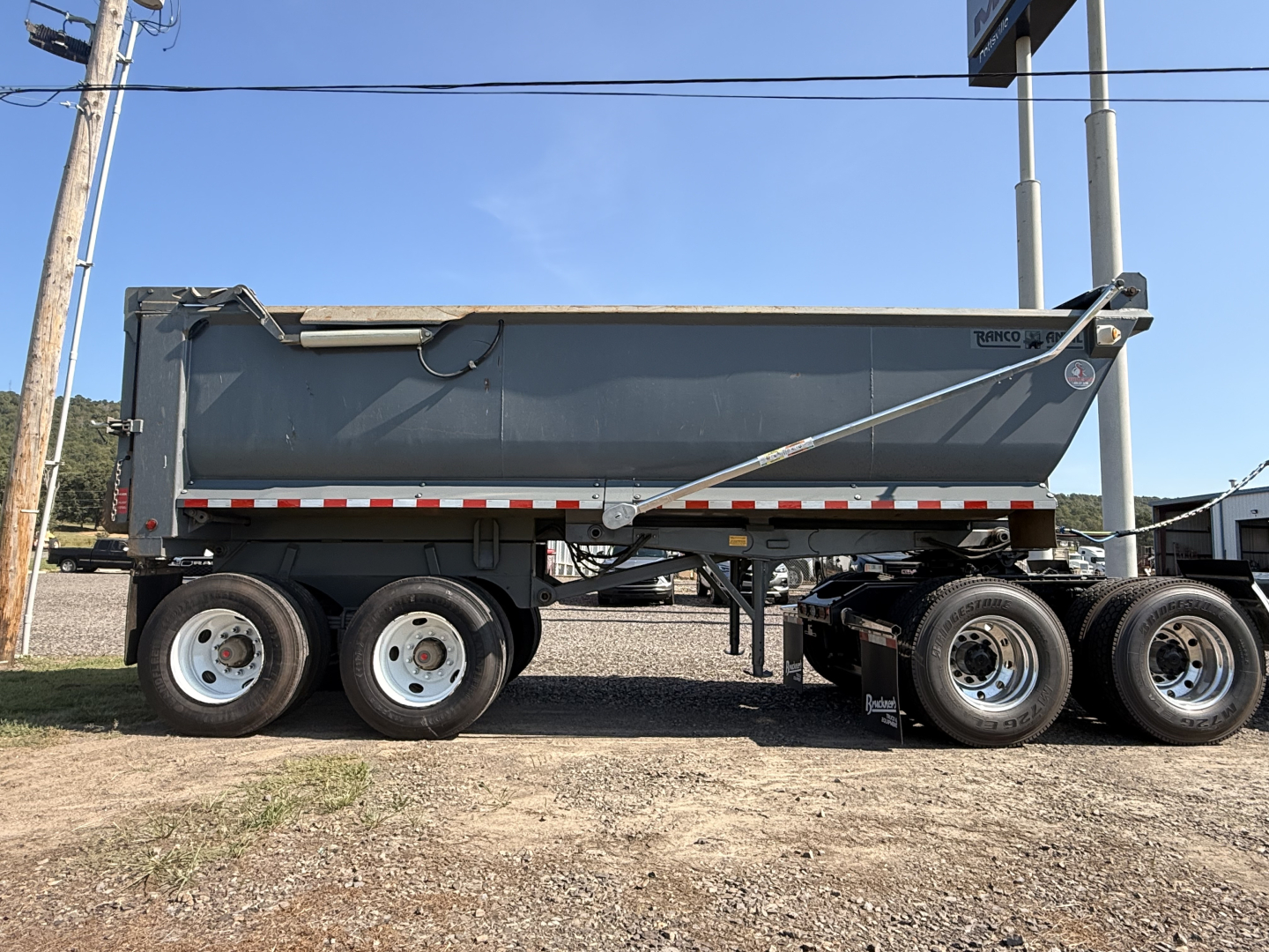 End dump trailer side view showing side panel with reflective stripe and Triple axle configuration.