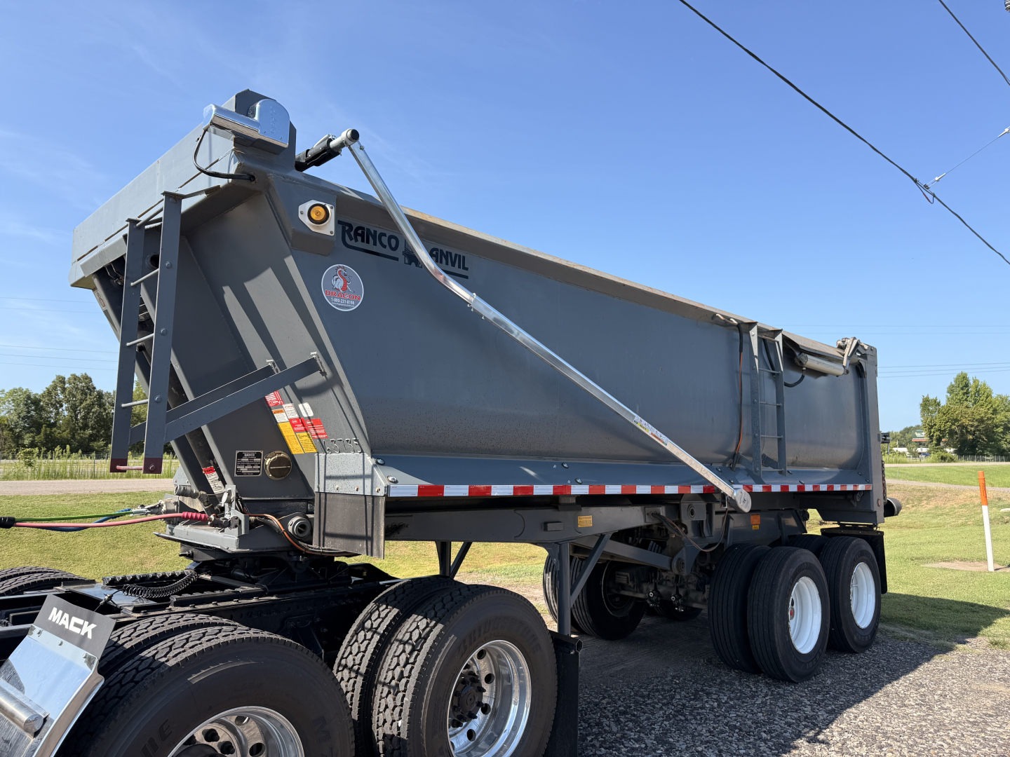 Dump trailer showing Ranco END DUMP logo and side panels with reflection; twin rear axles and hydraulic mechanism visible.