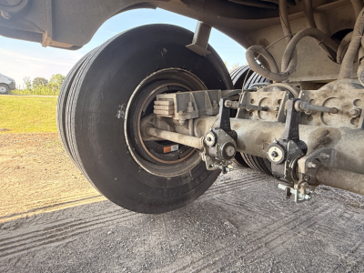 Trailer axle showing wheel and suspension components with bolts and air line fittings visible.