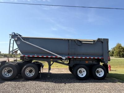 Dump trailer side view showing Ranco END DUMP with multiple axles and hydraulic tailgate; grey body, black undercarriage, white wheels, red/white reflective tape.