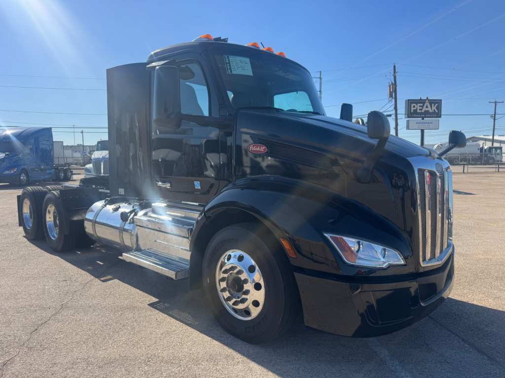 Peterbilt 579 conventional daycab truck in dark blue, side view, chrome fuel tanks and dual rear axles, cab with stepped aerodynamic design and long hood.
