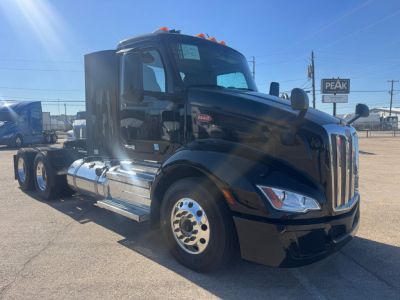 Peterbilt 579 conventional daycab truck in dark blue, side view, chrome fuel tanks and dual rear axles, cab with stepped aerodynamic design and long hood.