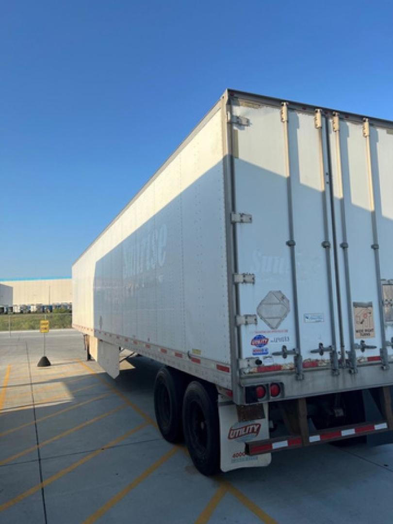 Rear view of a white utility van trailer showing dual rear axles and rear doors with latches.