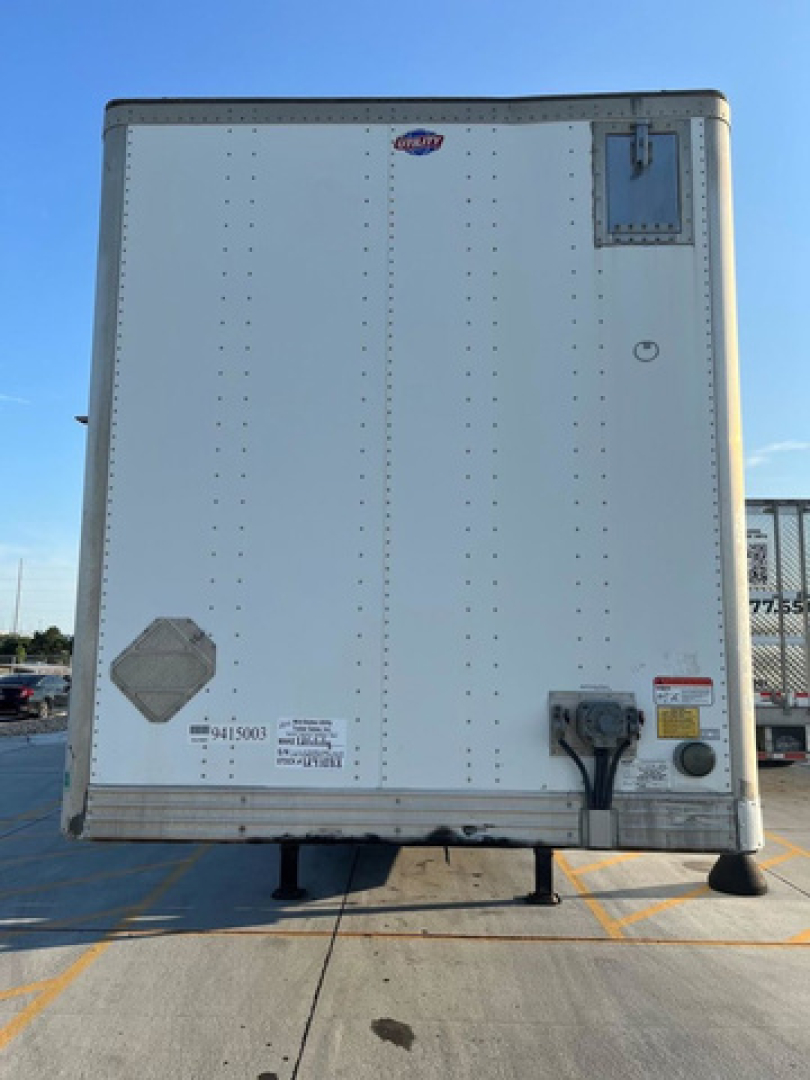 Rear view of a white utility trailer trailer in-service showing cargo door hardware and safety stickers.