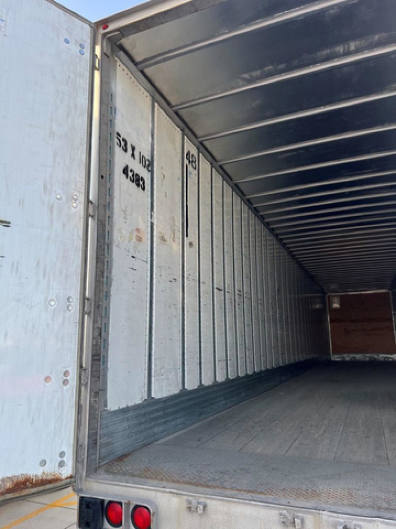 Utility van trailer interior with empty cargo area, metal side walls, open rear doors, and floor planks visible.