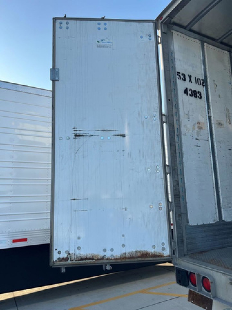 Utility van trailer open rear doors showing interior cargo area with metal walls and suspended floor; visible markings include weight and size text on right door.