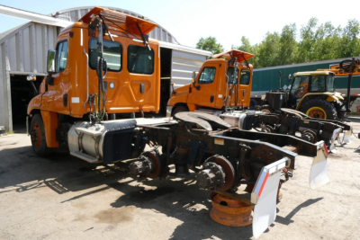 Freightliner Cascadia 125 truck chassis and cab with orange paint, no body on frame showing drive axles and suspension.