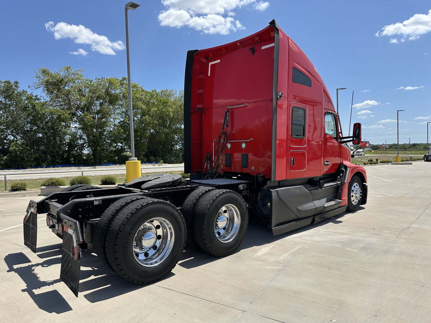 Kenworth T680 sleeper cab tractor with red exterior, rear and side view showing dual rear axles and fourth wheel, chrome rims, and black chassis components.