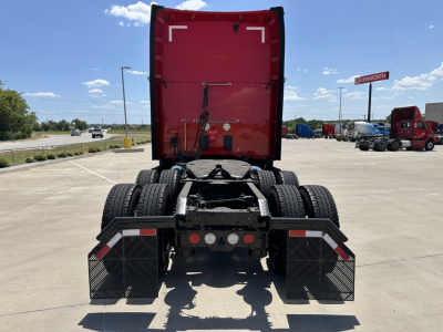 Kenworth T680 tractor rear view showing third axle and dual fuel tanks with mud flaps and rear lights.