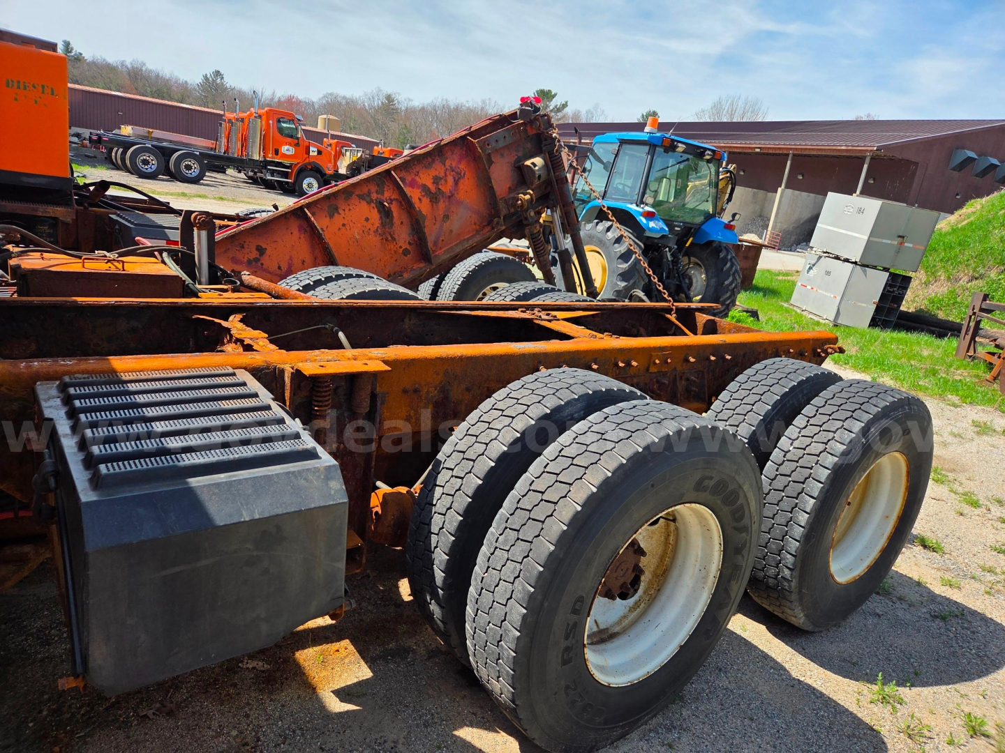 Chassis of a used 2006 International 7400 with dual rear axles and rusty loader attachment, tires visible, blue tractor in background.