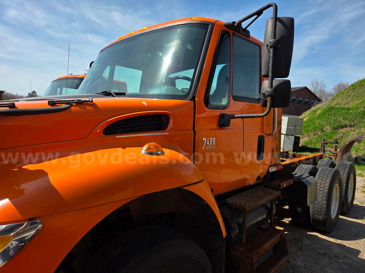 International 7400 cab and chassis showing orange truck with side steps and dual rear wheels.