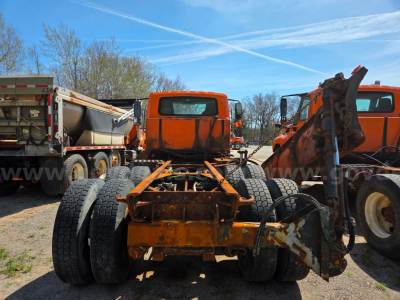 Chassis of a used 2006 International 7400 with orange frame, dual rear axles, and front hitch/frame components visible in a junkyard setting.