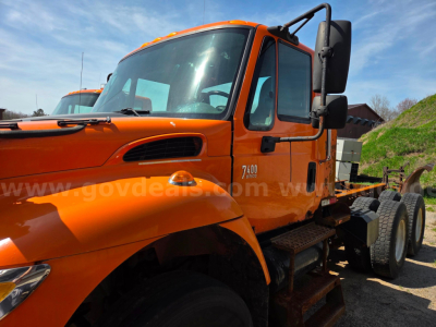 International 7400 cab and chassis showing orange truck with side steps and dual rear wheels.