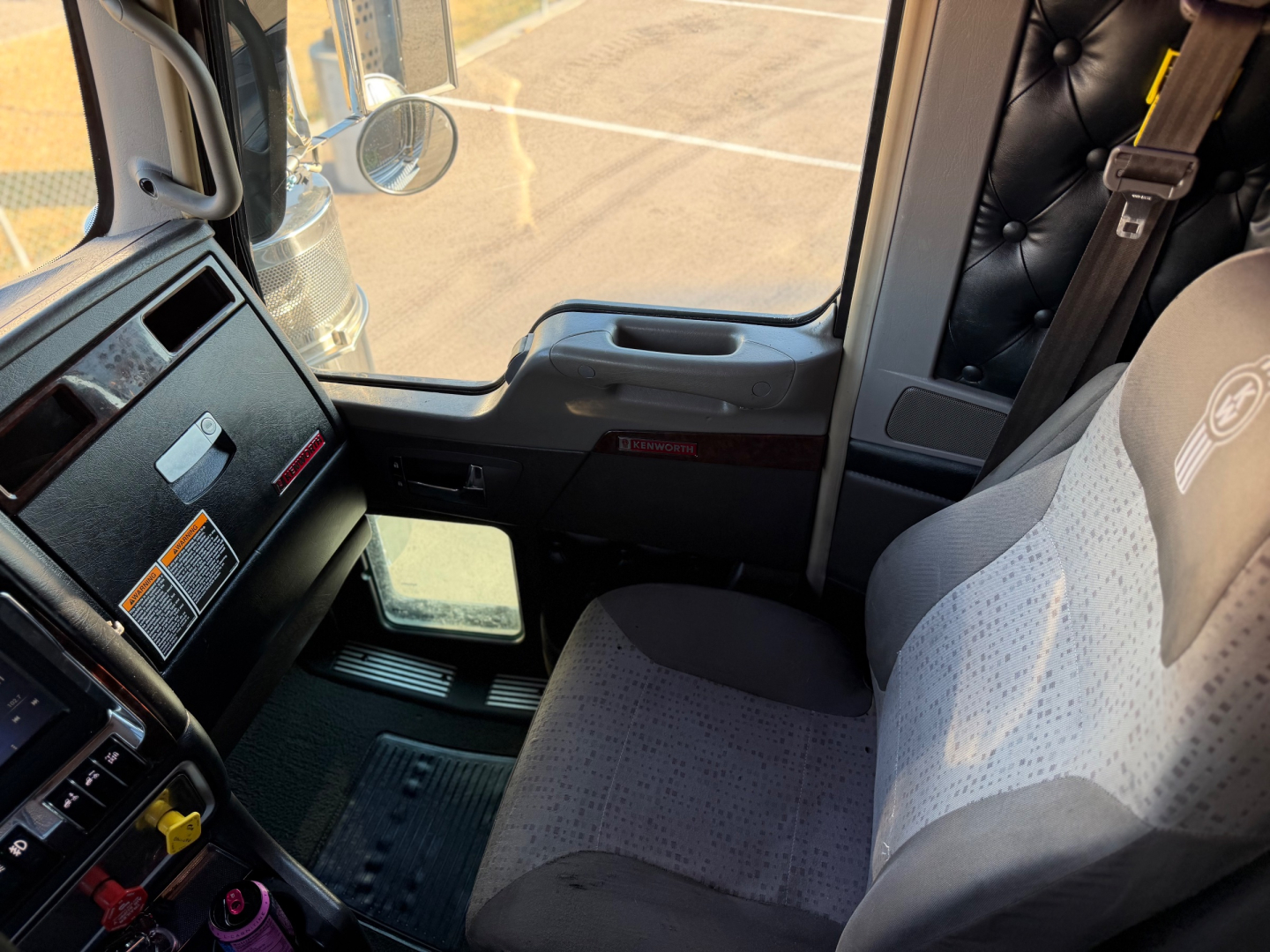 Kenworth W900L cab interior showing dashboard with steering wheel, seat, and window view.