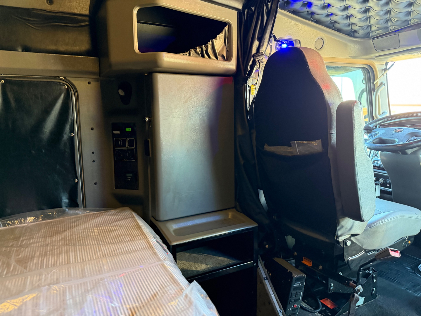 Kenworth W900L truck cabin interior showing driver seat, sleeper area, and dashboard with overhead storage.