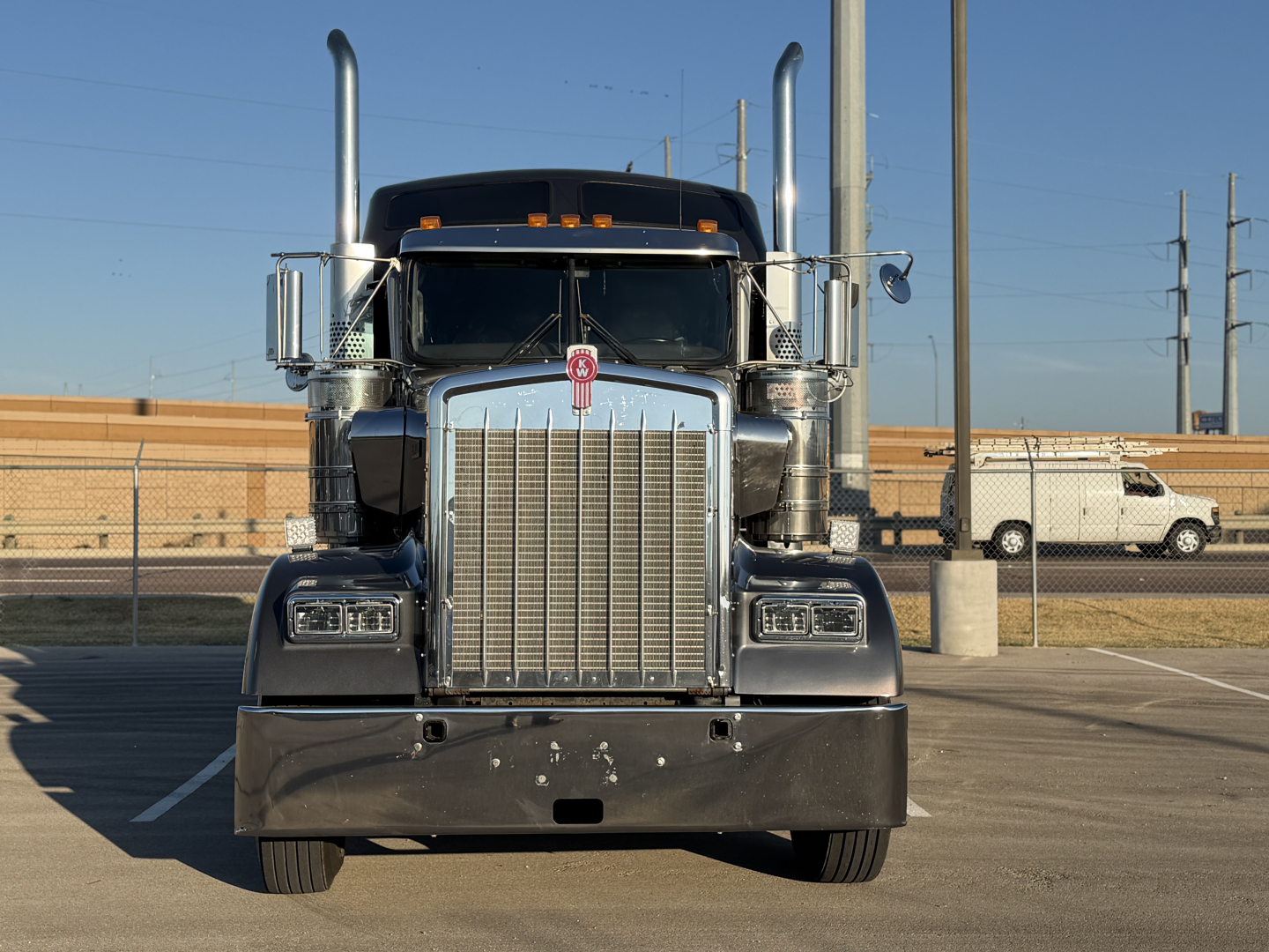 Kenworth W900L front view showing chrome grille, dual exhaust stacks, and large bumper with emblem.