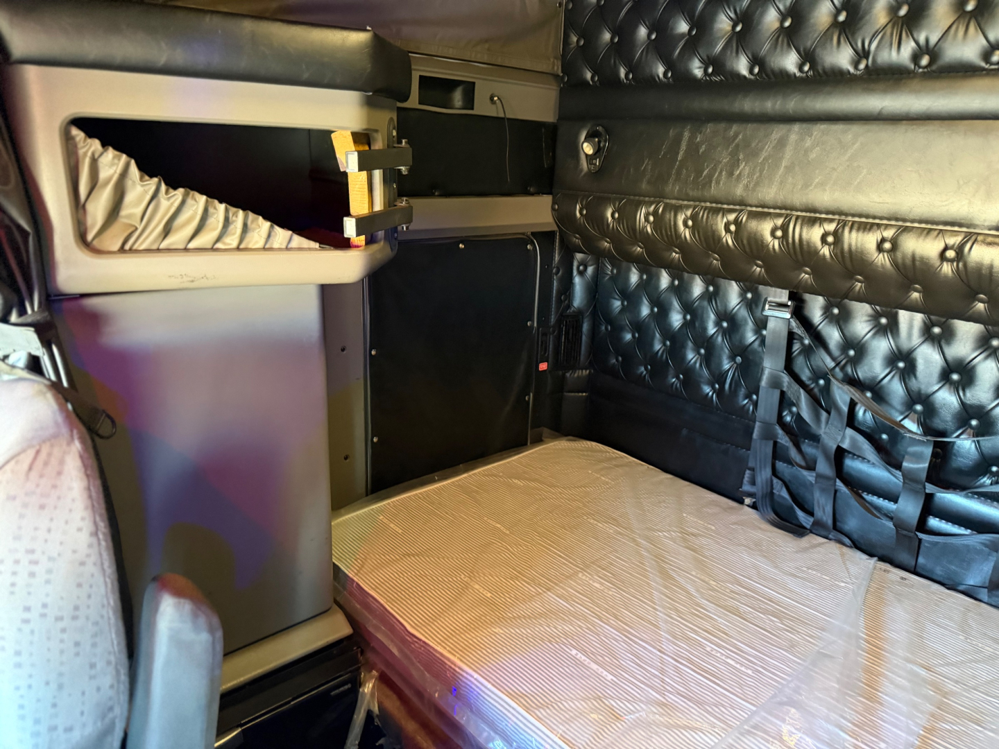 Kenworth W900L sleeper cab interior showing quilted black side panels and light-colored sleeper area with storage compartments and seating.