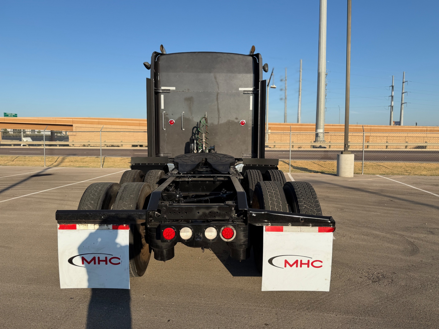 Kenworth W900L tractor rear view showing dual rear axles and mud flaps with MHC logo.