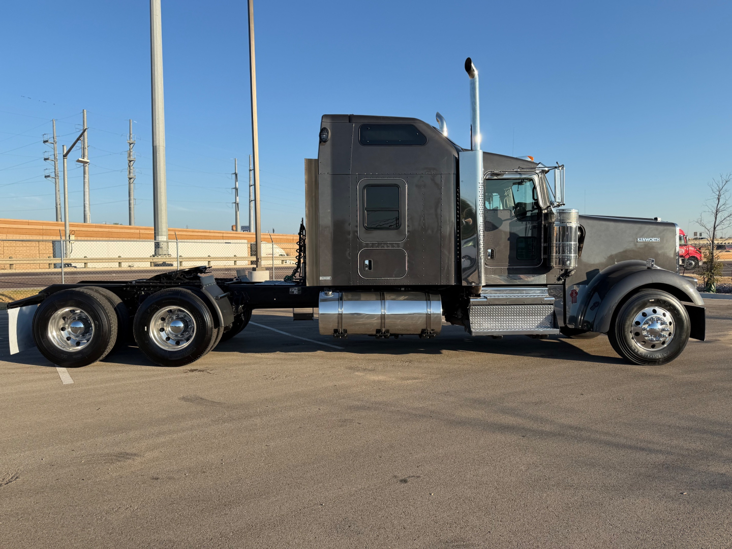 Kenworth W900L semi-truck side view showing black cab, dual rear axles, chrome exhaust stack, and fuel tanks.