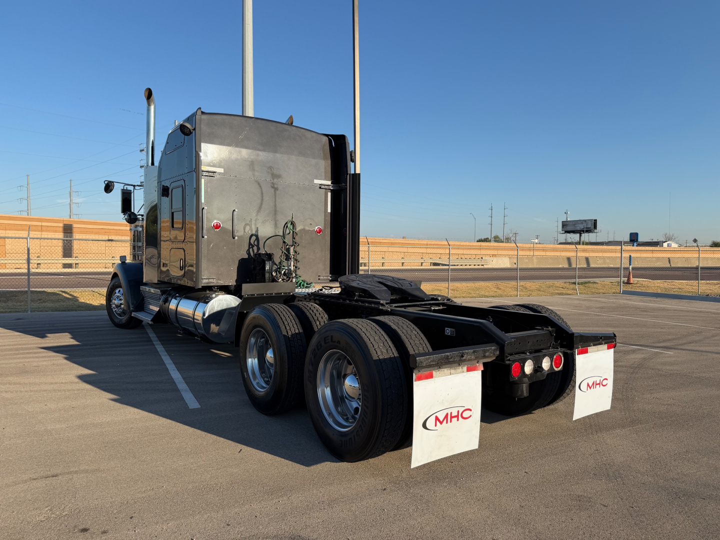 Kenworth W900L semi-truck rear and cab, chrome exhaust stacks, dual rear axles, mudflaps with MHC logo.