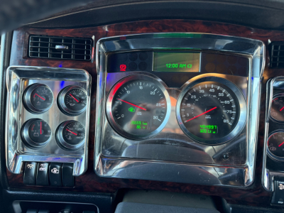 Kenworth W900L dash cluster showing multiple gauges and center digital clock, with woodgrain trim and chrome surroundings.