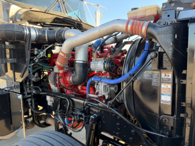Kenworth W900L engine bay showing V8 engine with red and blue hoses, radiator, intercooler piping, and PACCAR branding.