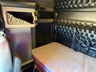 Kenworth W900L sleeper cab interior showing quilted black side panels and light-colored sleeper area with storage compartments and seating. 