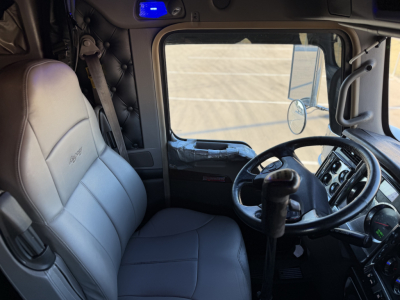 Interior of a Kenworth W900L truck cab showing steering wheel, seats, and dashboard with light gray upholstery.