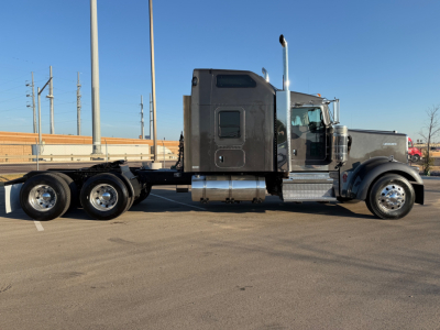 Kenworth W900L semi-truck side view showing black cab, dual rear axles, chrome exhaust stack, and fuel tanks.
