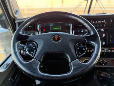 Kenworth W900L steering wheel and dashboard view in cab, with instrument cluster and control stalks visible.