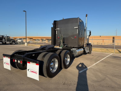 Kenworth W900L truck tractor in a lot, rear three-quarter view, tandem axles, sleeper cab, fuel tanks, mud flaps with MHC logo.