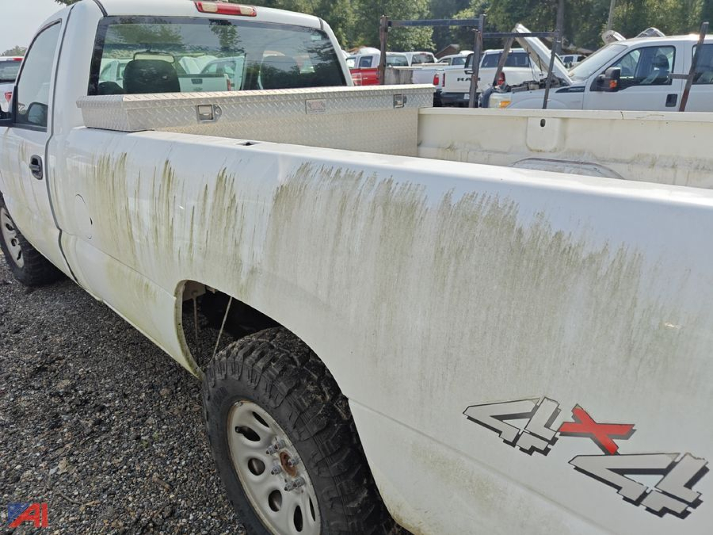 Truck bed of a white 2006 GMC Sierra 1500 pickup showing dirt splatter and 4x4 decal on rear fender, utility bed in background.