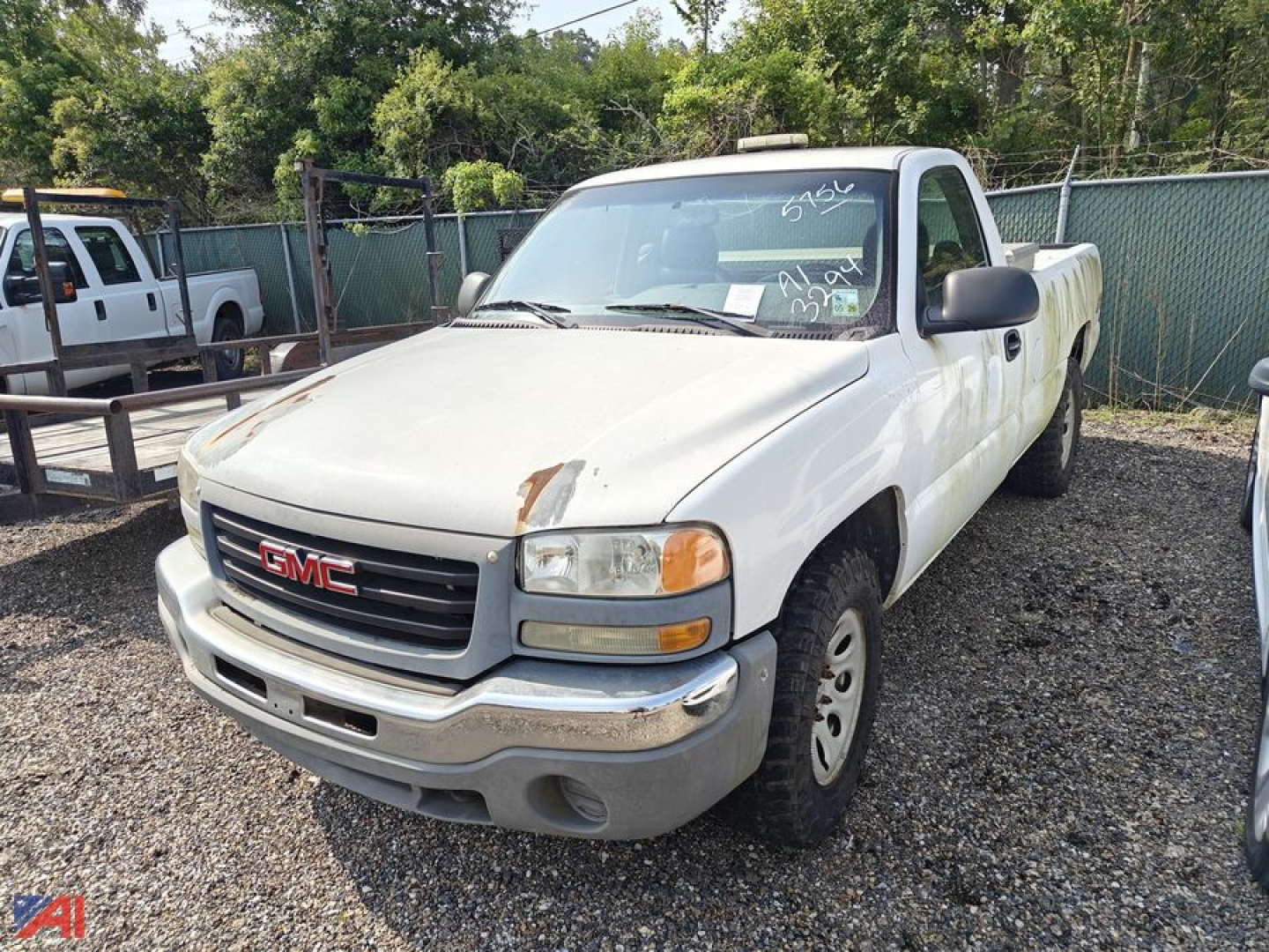 GMC Sierra 1500 pickup truck in a lot, white two-door reg cab with front bumper, grille, headlights, and a long bed; appears used with some wear.