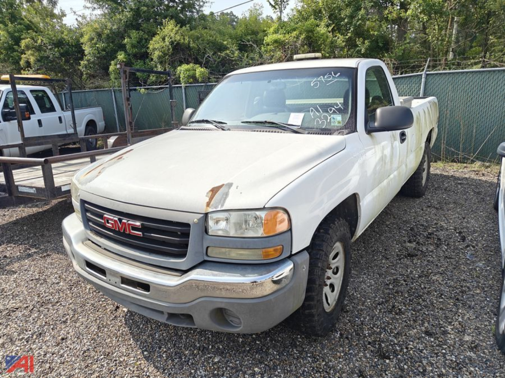 GMC Sierra 1500 pickup truck in a lot, white two-door reg cab with front bumper, grille, headlights, and a long bed; appears used with some wear.