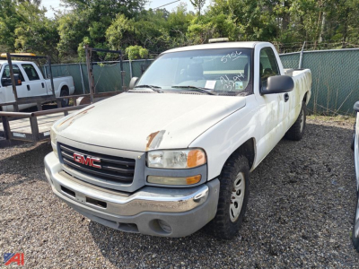 GMC Sierra 1500 pickup truck in a lot, white two-door reg cab with front bumper, grille, headlights, and a long bed; appears used with some wear.