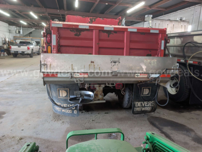 Rear view of a red 2006 International 7400 dump truck in a workshop, showing the metal tailgate, mud flaps with Devers Truck Wood, and undercarriage details.