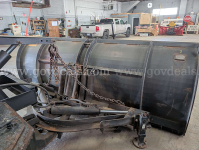 Dump truck equipment in a workshop with a large snowplow blade and hydraulic components visible.