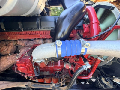 Engine bay with red components and blue hose clamp, showing exhaust manifold and intake piping in a Mack Granite dump truck engine area.