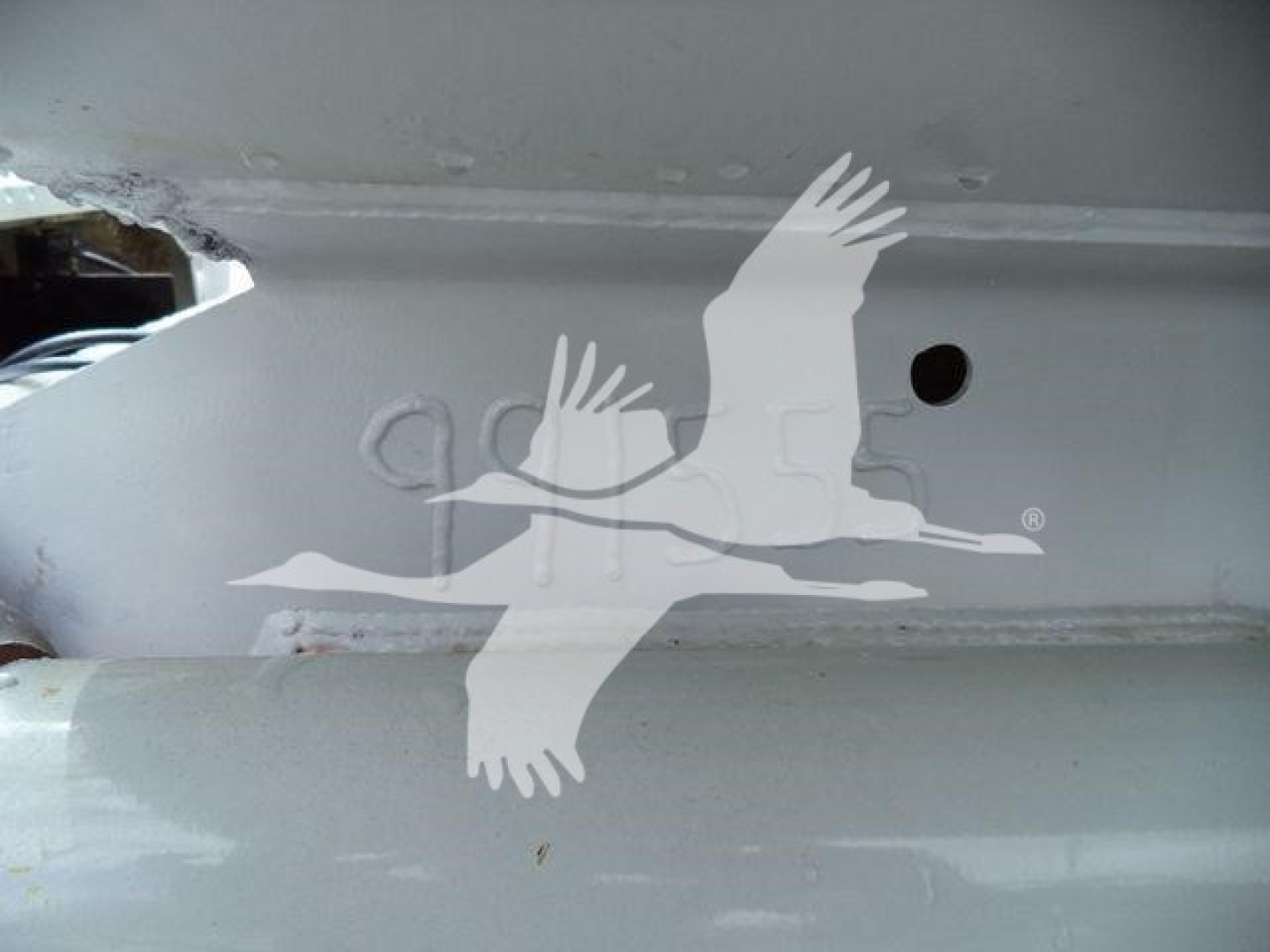 Image shows a metal truck frame with a bird decal overlay. Partial view of a hole and surface features. No distinct labels visible.
