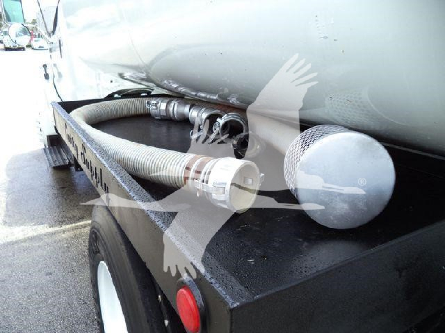Hose and connection fittings on a fuel or liquid tank rear side of a truck trailer, with a large cylindrical tank and hose reel visible.