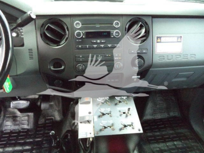 Dashboard and center console of a Ford F-650 Super Duty with a mounted aluminum control panel under the dash showing various switches; steering wheel on left, 'SUPER' badge on passenger side, instrument cluster center, and floor mats visibl