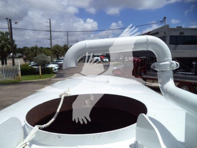 Open-top cylindrical tank with large white curved piping system on top, truck trailer in background; circular manhole opening visible; white rope; industrial vehicle components.