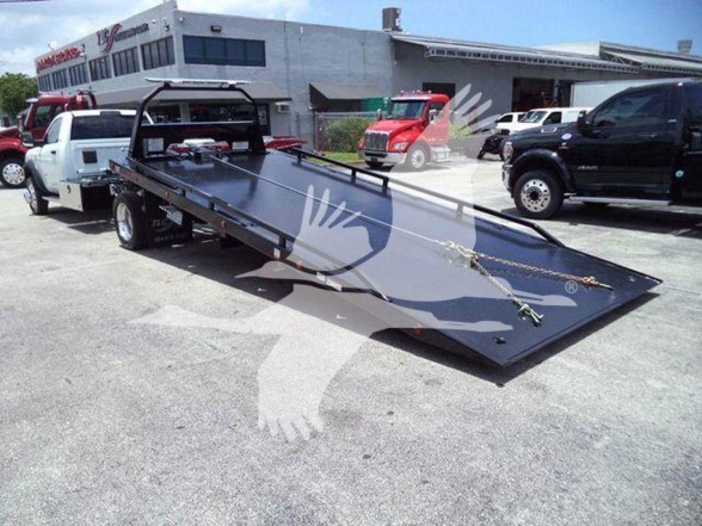 Ram 5500 rollback tow truck with a heavy tilt bed and winch mounting points in a dealership lot.