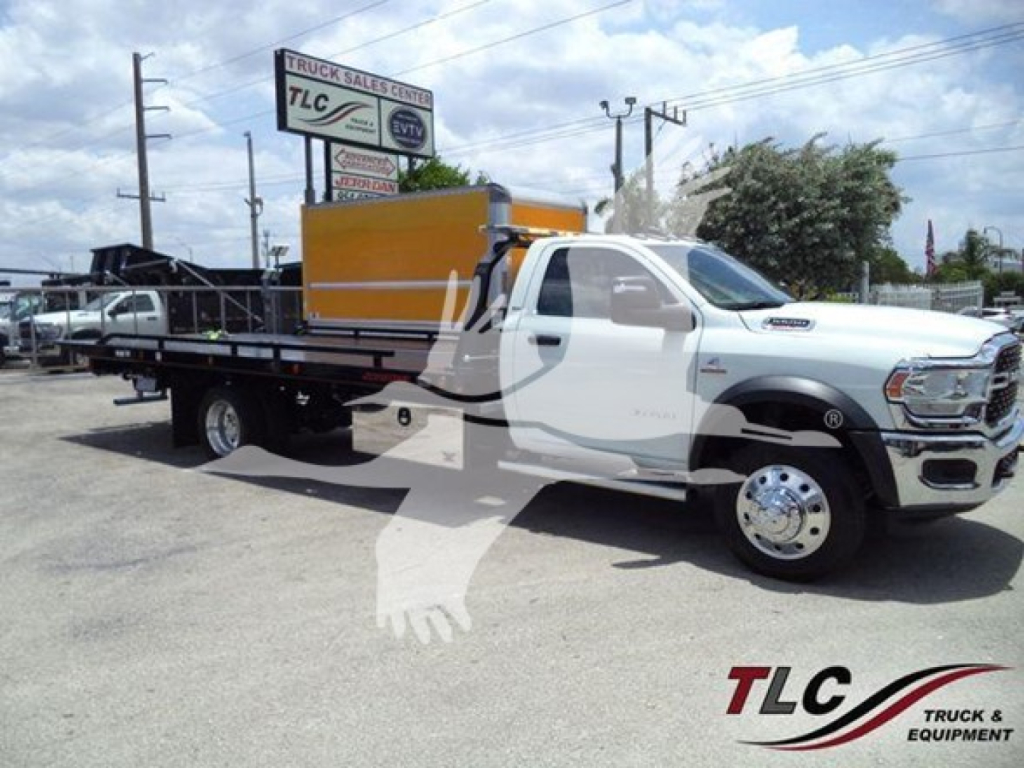 Ram 5500 rollback tow truck in white with black flatbed and orange toolbox, front cab, dealership lot in background.