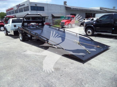 Ram 5500 rollback tow truck with a heavy tilt bed and winch mounting points in a dealership lot.
