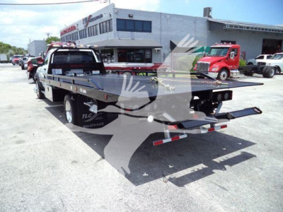 Ram 5500 rollback tow truck flatbed view showing rear with ramps and dual axles, dealership lot in background.